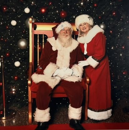 Santa Michael and Mrs. Claus together by a sparkling Christmas tree